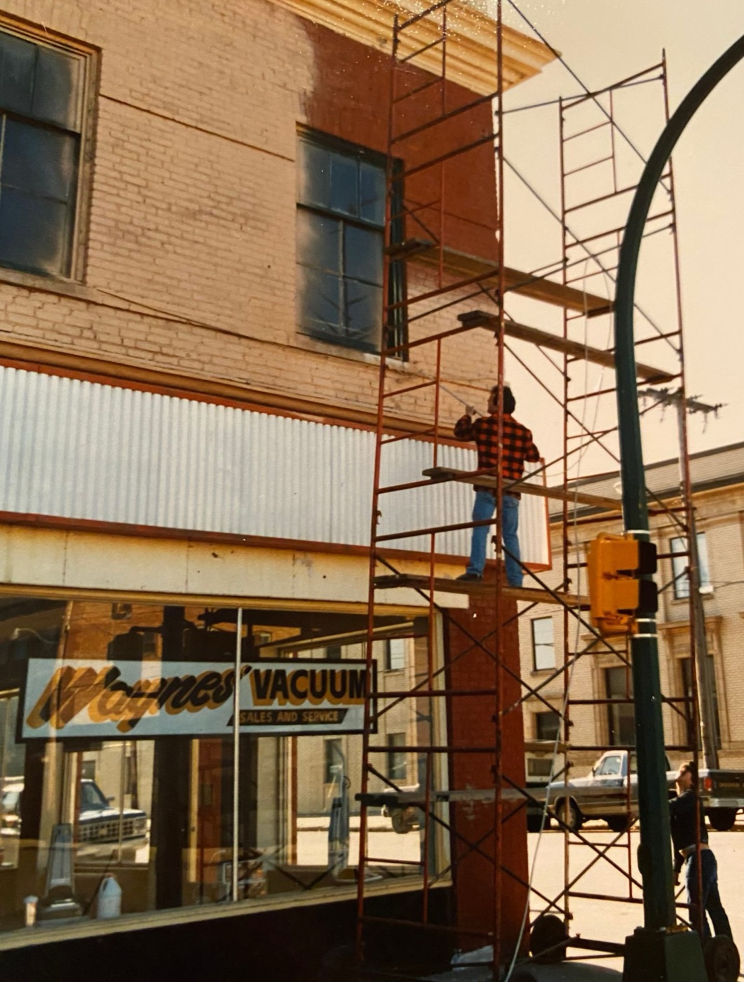 Painter on red scaffolding repainting the upper floor of a brick storefront